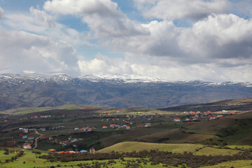 Obraz premium A village on the slopes of the mountain, cloudy sky, meadows and trees
