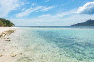 A tranquil beach showcases crystal-clear water reflecting the sky, with soft white sand stretching along the shore, perfect for relaxation and exploration.