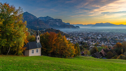 little Chapel, Panorama Sunset over Rhine Valley, blue sky over the city of Dornbirn, meadow and fields. autumn colored trees. beautiful afterglow, interesting colored veil clouds over Swiss mountains