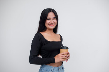 A pretty southeast asian woman smiling, dressed casually in a black long-sleeve crop top, ripped jeans. Holding a cup of coffee. Isolated on a white background.