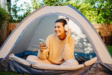 Young woman listening to music or audio book in tent in backyard	