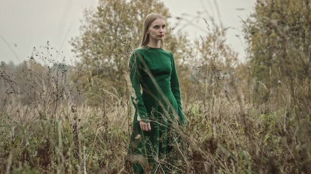 Woman modeling a green dress stands gracefully in a field, striking poses for the camera. The natural setting enhances her elegant look, showcasing the beauty of fashion in an outdoor environment