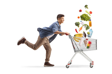 Full length profile shot of a guy running fast with a shopping cart with groceries falling inside