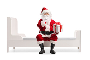 Santa Claus holding a surprise present box and sitting on a bed