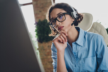 Photo of doubtful unsure lady broker wear shirt spectacles earphones working modern gadget indoors workplace workshop