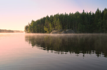 Lake in Sweden at sunrise with romantic light, blue water and trees on the shore