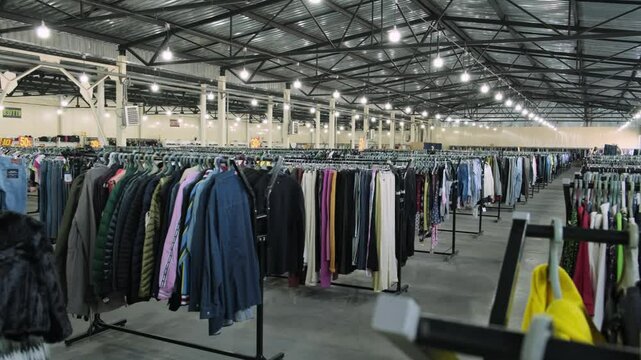 Large second-hand clothing store interior with numerous racks of diverse clothing under bright industrial lights.