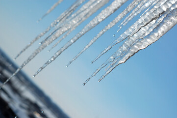 icicles against the background of a clear blue sky above the city, drops melt from the icicles