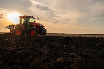 Obraz premium Tractor on the field during sunset.