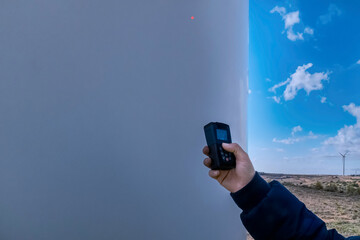 Hand holding electronic device inspecting wind turbine for renewable energy