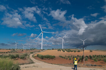 Engineer walking near solar panel and inspecting wind turbines in countryside