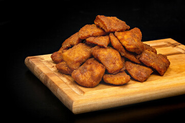 Meat slices fries on a wooden board, on a black background. Beer snack.