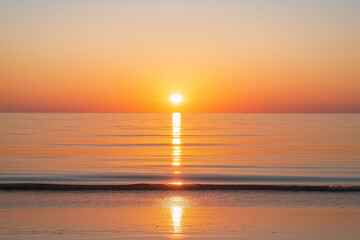 Sunset over the calm ocean with a golden sky casting a warm glow over the water, creating a tranquil and breathtaking seascape.