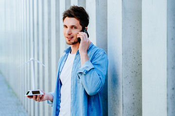 Young man talking on phone while holding wind turbine model