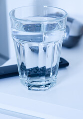a glass of water on the nightstand table, reflecting the remote and bedside clock