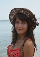 A young beautiful dark-skinned girl with blue eyes wearing a hat. Portrait of a woman in a swimsuit against the background of the sea.