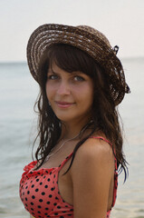A young beautiful dark-skinned girl with blue eyes wearing a hat. Portrait of a woman in a swimsuit against the background of the sea.