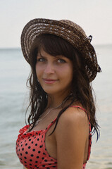 A young beautiful dark-skinned girl with blue eyes wearing a hat. Portrait of a woman in a swimsuit against the background of the sea.