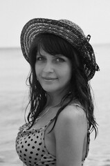 Black and white portrait of a beautiful young dark-haired girl against the backdrop of the sea. Woman in a hat and polka dot swimsuit. Summer, beach, tourism advertising.