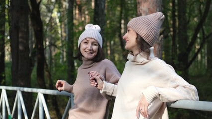 Two girlfriends or sisters in knitted hats are walking outside in an autumn park. Young women...