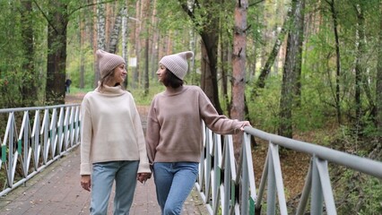 Two girlfriends or sisters in knitted hats are walking outside in an autumn park. Young women enjoying the beautiful weather while walking