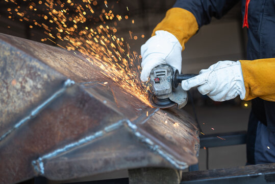 Metal worker using angle grinder creating sparks during polishing metal structure