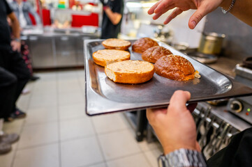 Close-up of hands holding a tray with freshly toasted buns in a busy kitchen. Ideal for themes related to food preparation, cooking, or restaurant service