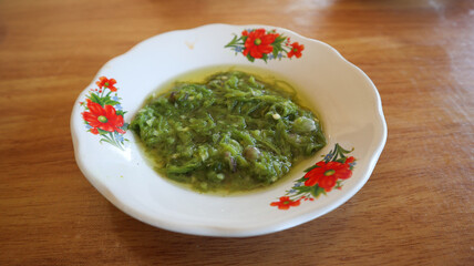 Selected focus Green Chilli Paste or sambal cabe hijau, made by chilli, garlic, salt and sugar. Top View of Sambal Lado Mudo or sambal Cabe Ijo. minangkabau food served on white plate