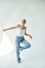 A young bald woman exudes confidence and joy while standing playfully in stylish jeans.