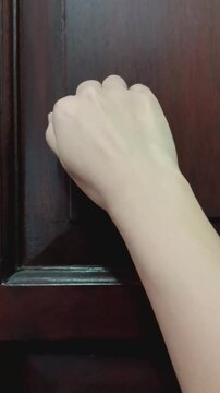 Woman's hand knocking fist on wooden door.