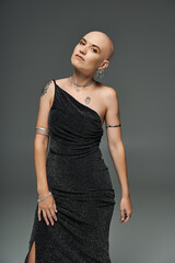 A young bald woman confidently poses in a shimmering gown, radiating beauty and grace.