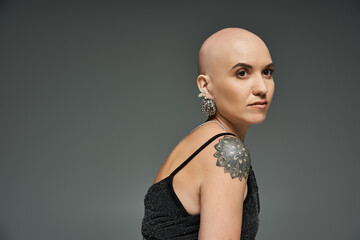 A young bald woman radiates strength and elegance, adorned with striking jewelry and a tattoo.