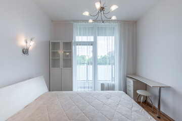 Wide Angle of Home Bedroom Interiom. King Size Double Bed and Windows, Door to Balcony in Background. White Walls. Family Home. Windows And Curtains. Desk and Chair