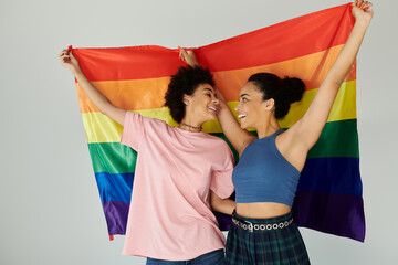 Two friends embrace and smile while holding a colorful pride flag, radiating joy and unity.