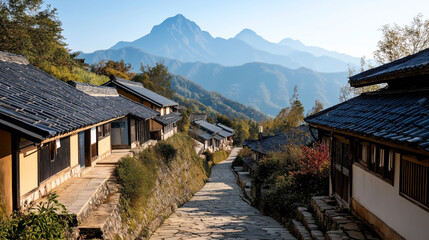 Fototapeta premium Traditional mountain village pathway with stone houses and tile roofs surrounded by lush greenery and scenic mountain views in the background under a clear sky. Serene rural landscape.