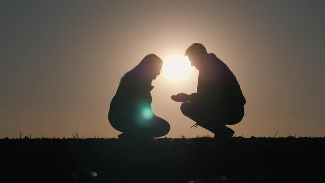 A pair of farmers in a field examining a soil sample. Silhouetted in the rays of the setting sun