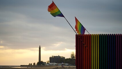 Winter Pride Maspalomas. Rainbow flags on the kiosk bar of the Gay beach of Maspalomas waving in front of the lighthouse at sunset