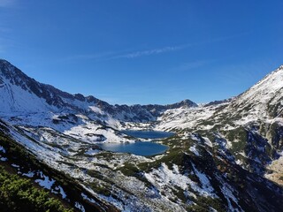 An unparalleled view of a crystal-clear lake in the Valley of Five Ponds, Tatra Mountains, Poland, reveals stunning alpine beauty, surrounded by rugged peaks and lush greenery