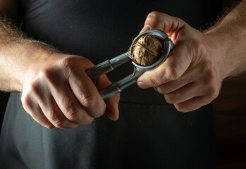 A chef peels a walnut with a nutcracker. A low-key concept for cooking with walnuts