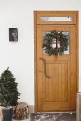 Stylish christmas rustic wreath with ribbon hanging on front doors, close up. Modern house entrance...