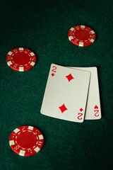 A pair of two diamonds lies on the green felt, surrounded by vibrant red poker chips, creating a tense atmosphere of anticipation and strategy at the card table