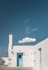 A charming Cycladic house in Greece showcases its distinctive white architecture and a vibrant blue door against a stunning clear sky with a single cloud drifting by.