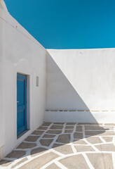 A striking example of traditional Cyclades architecture, this space showcases whitewashed walls and a blue door under bright sunlight, creating a serene atmosphere.