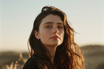 Fototapeta premium A young woman in a sun-kissed field looks into the distance, her expression reflecting thoughts of freedom and dreams.