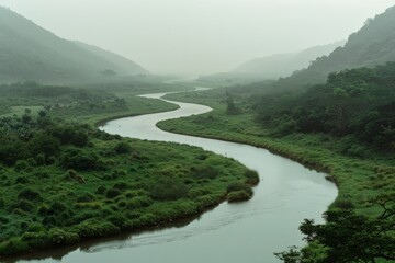 A winding river snakes through lush, verdant valleys under a misty, overcast sky, offering a serene and picturesque landscape view.