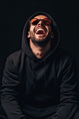 Fototapeta premium in black sunglasses in a tracksuit on a plain background. strong happy emotions. laughter. different tones dark black background. 