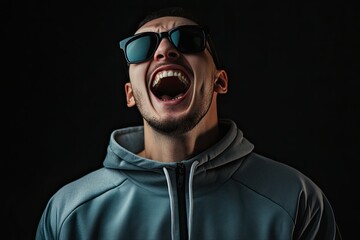 Obraz premium in black sunglasses in a tracksuit on a plain background. strong happy emotions. laughter. different tones dark black background. 