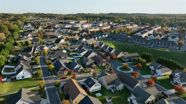 New developed american housing area with modern single family homes in suburb. Sunset time on Beautiful autumnal day in USA. Colorful trees on streets. Aerial descend wide shot.