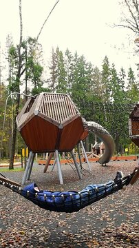 A boy in a blue jacket and jeans lies and rests in a hammock on a playground in the autumn Borovsky Park in Moscow.