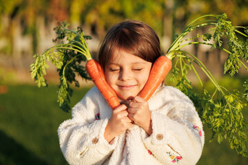 little girl farmer with vegetables and pumpkin on the background of green grass and vegetable garden. healthy eating concept.